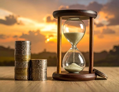 Hourglass and stacked golden coins, illustrating currency fluctuation and time impact commodities