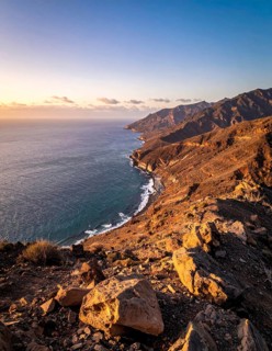 Desert landscape converges with ocean along a rugged coastal area, shore break at cliffs, blue