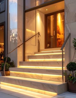 Modern building entrance with stairs, glass facade, and plants in warm evening light, empty