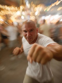 A man gets into a fighting stance, surrounded by dynamic movement and a background filled with