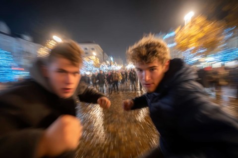Two men in fighting pose on a rainy street at night, surrounded by lights, symbolic image for