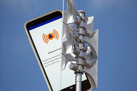 (Photomontage) Close-up of a siren, next to it the open warning app NINA on a smartphone