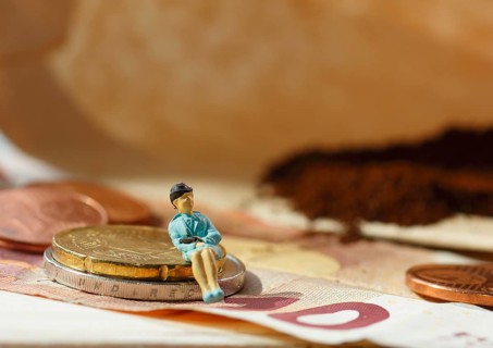 Miniature figure of a woman sitting on coins and banknotes, ground coffee in a filter bag in the