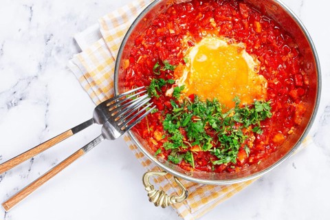 Traditional Turkish dish, scrambled eggs with tomatoes, Menemen, with herbs, in a frying pan,