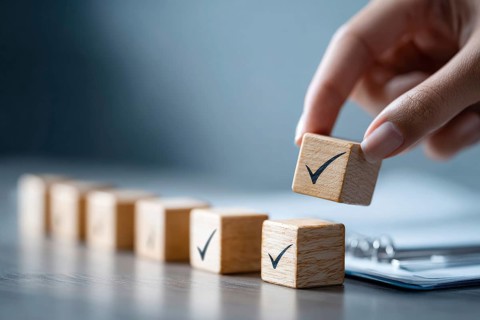 Checklist and task progress tracking concept. A hand placing the final checkmark on wooden blocks