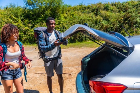 Young couple of hikers preparing their backpacks for an exciting road trip, opening the car trunk