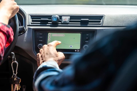 Close up of passenger using navigation system on car dashboard while driver operates steering wheel