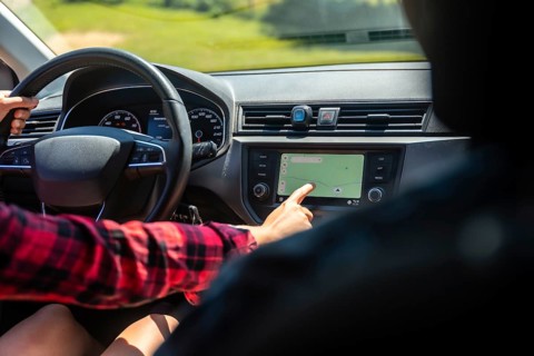 Woman driving a car while interacting with the navigation system on the dashboard's touchscreen