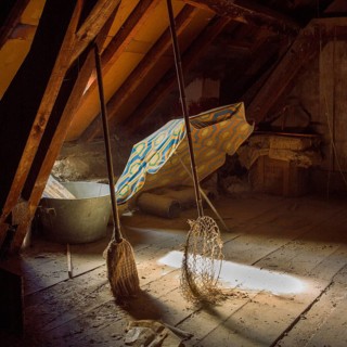 Sunlight filters through an attic, illuminating a colorful sunshade and a butterfly net alongside