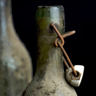 Three dusty vintage bottles stand together, covered in grime, highlighting their age and history.