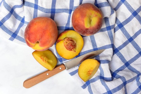 Peach with knife on kitchen towel, peach halves, Prunus persica