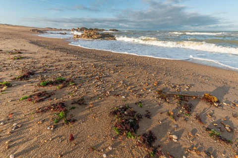 The waves crash gently against a rocky shoreline at sunset, creating a tranquil atmosphere. The