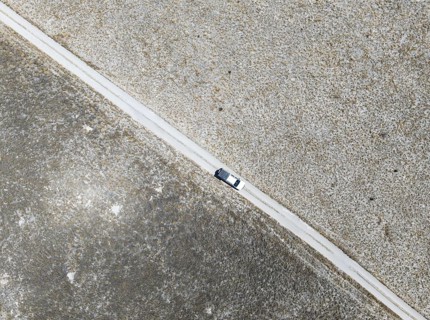 Off-road vehicle driving on a sandy track through a vast dry landscape with yellow grass, Top Down,