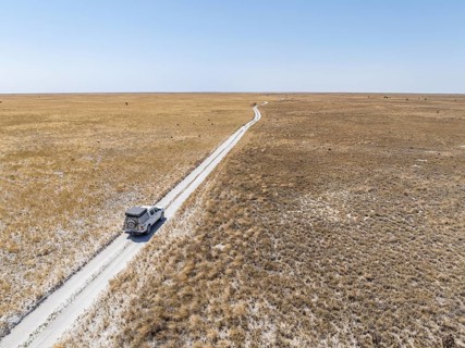 Off-road vehicle driving on a sandy track through a vast dry landscape with yellow grass, Sowa Pan,