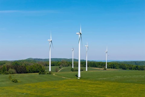 Wind turbines on a green field surrounded by forest under a blue sky, Swabian Alb,