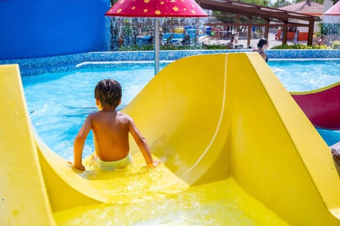 Young boy enjoying a thrilling ride down a vibrant waterslide at a lively water park, embracing the
