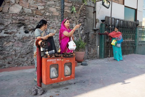 Indian woman holding tea lights in the air at a fire hydrant, Govind Dev Ji Hindu temple in the old