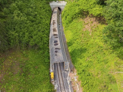 A train emerges from a tunnel, surrounded by green nature, construction of the Hermann Hesse