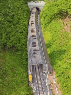 Aerial view of a railway tunnel stretching through green hills and a dense forest, construction of