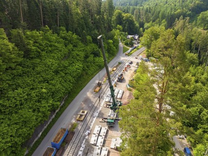 Construction work with a crane along railway tracks, surrounded by forest, construction of the