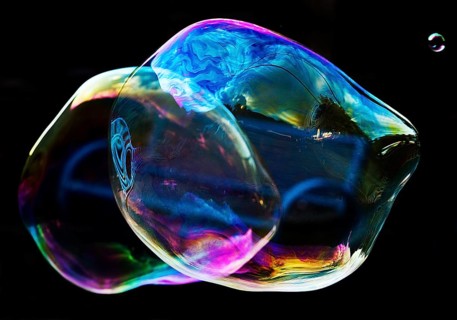 Irregular, iridescent soap bubble in the colours of the rainbow against a black background,