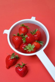 Strawberries in a colander on a red background, Fragaria