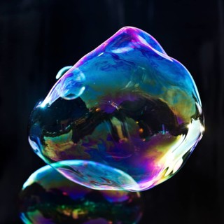 Large, irregular, iridescent soap bubbles in the colours of the rainbow against a black background,
