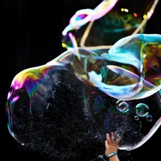 A hand bursts a large iridescent soap bubble against a black background, Recklinghausen, Germany