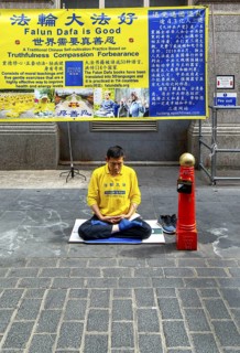 Falun Dafa or Falun Gong man meditating sitting cross legged, Gerrard Street, Chinatown, West End,