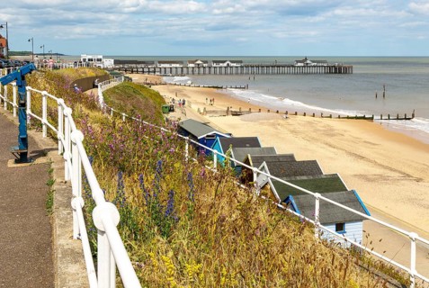 View over beach huts to sandy beach and pier, Southwold, Suffolk, England, UK