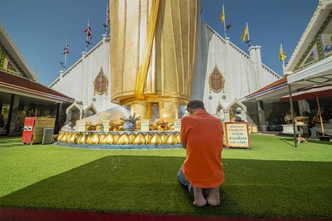 Man praying in front of a 32 metre high standing Buddha decorated with glass mosaics and 24 carat