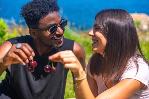 Young man and woman laughing together while sharing fresh cherries, savoring the joy of a sunny