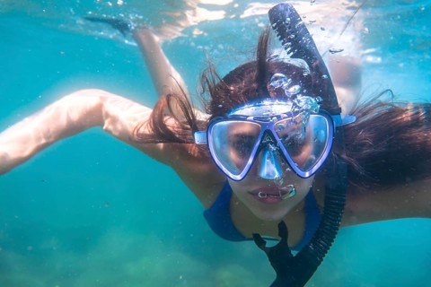 Tourist enjoys snorkeling in crystal clear ocean water, creating a stream of bubbles as she