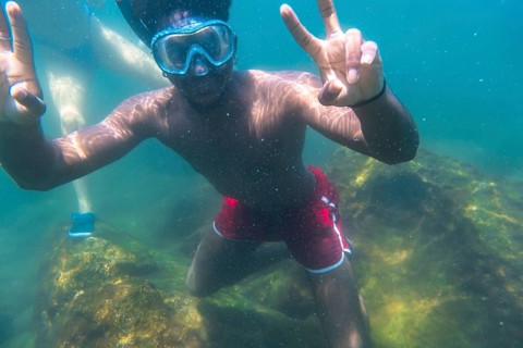 Young man snorkeling underwater, flashing the peace sign with both hands, enjoying the vibrant blue