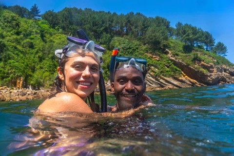 Interracial couple enjoying snorkeling adventure, embracing in refreshing ocean waters with scenic