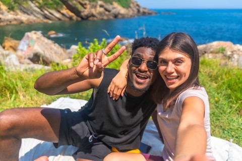 Young tourists enjoying a sunny day by the sea, sharing joyful moments while taking selfies and
