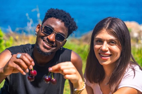 Interracial couple smiling while sharing fresh cherries, enjoying a sunny summer vacation by the