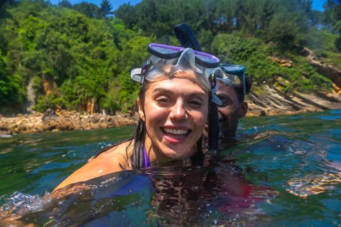 Interracial couple snorkeling together in the ocean, surrounded by a vibrant green coastline,