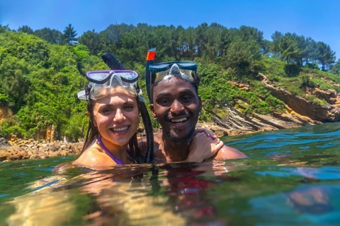 Interracial couple snorkeling in the clear blue sea, surrounded by a stunning green cliff, enjoying