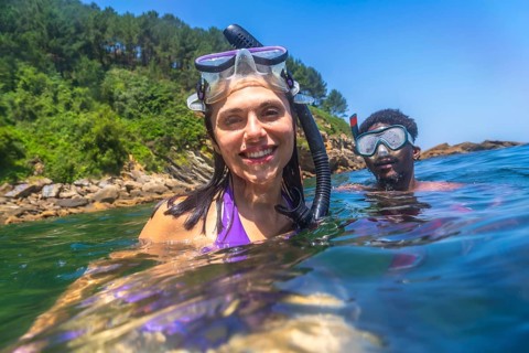 Happy couple snorkeling together in the ocean near the rocky coastline, enjoying their summer