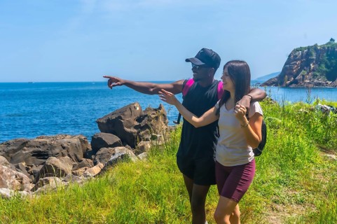 Interracial couple hiking along a stunning coastline, joyfully pointing at a breathtaking view in