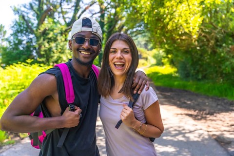 Interracial couple hiking on a sunny summer day, embracing each other and sharing joyful smiles
