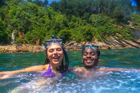 Interracial couple enjoying snorkeling in beautiful turquoise water with lush vegetation on the