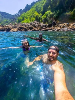 Three friends wearing snorkeling gear and enjoying the refreshing ocean water near a rocky coast