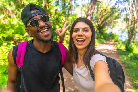 Interracial couple taking a selfie while hiking on a forest trail, enjoying their outdoor adventure