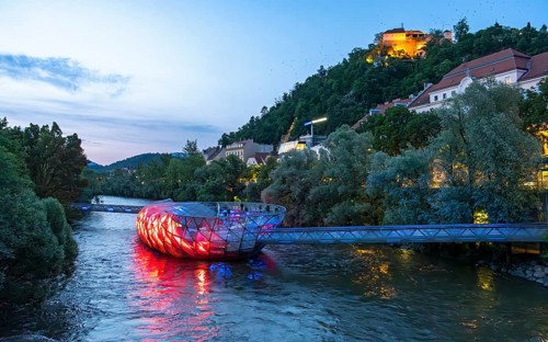Night-time view of the Murinsel floating island on the river Mur with Schlossberg castle hill in