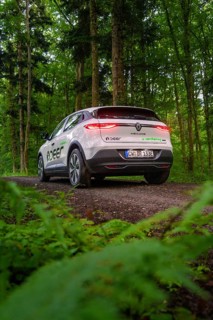Car on forest road with shining rear lights surrounded by dense green forest, Deer E- CarSharing,