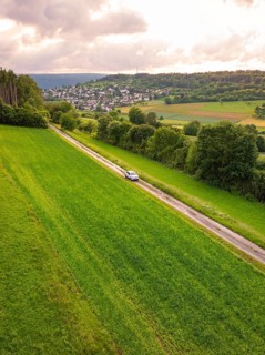 Car on a long journey through green fields, hills and villages in the background, Deer E-