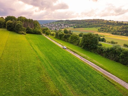 Car drives a straight road through wide green landscape with cloudy sky, Deer E- CarSharing,