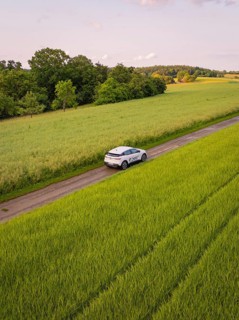 Car drives through rural route surrounded by green fields and summer landscape, Deer E- CarSharing,